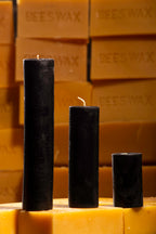 Three black slim beeswax pillar candles on a background of stacked natural beeswax blocks