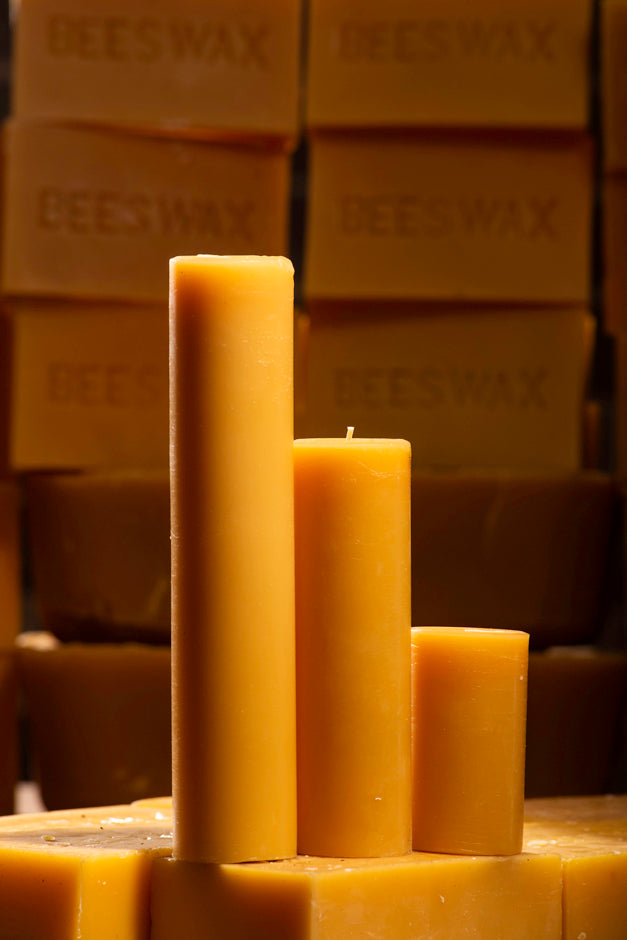Three natural slim beeswax pillar candles on a background of stacked natural beeswax blocks