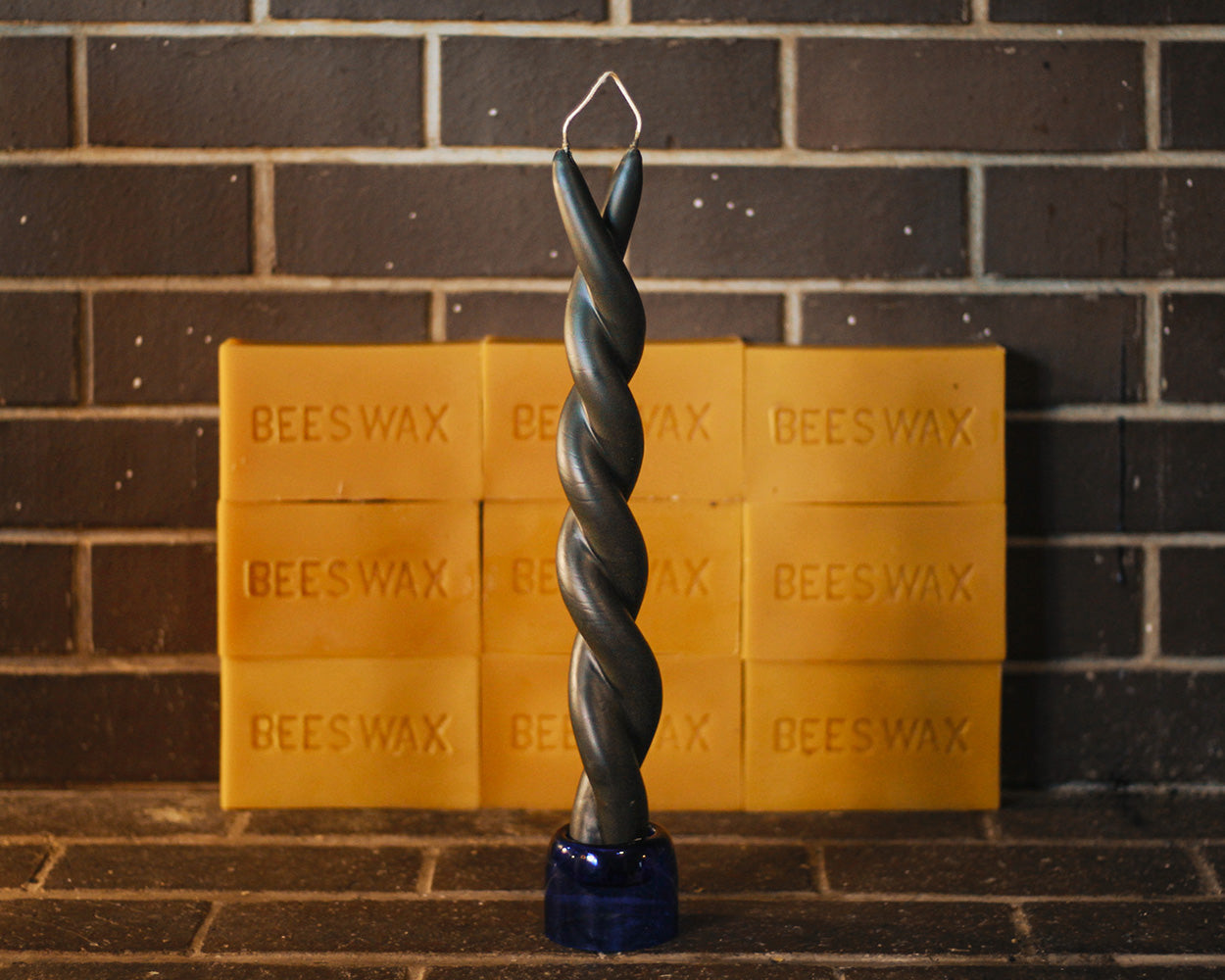 Twisted black beeswax candle on a stand with natural beeswax bars in the background.