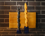 Two twisted beeswax candles in front of a brick wall with a block labeled 'Beeswax'.